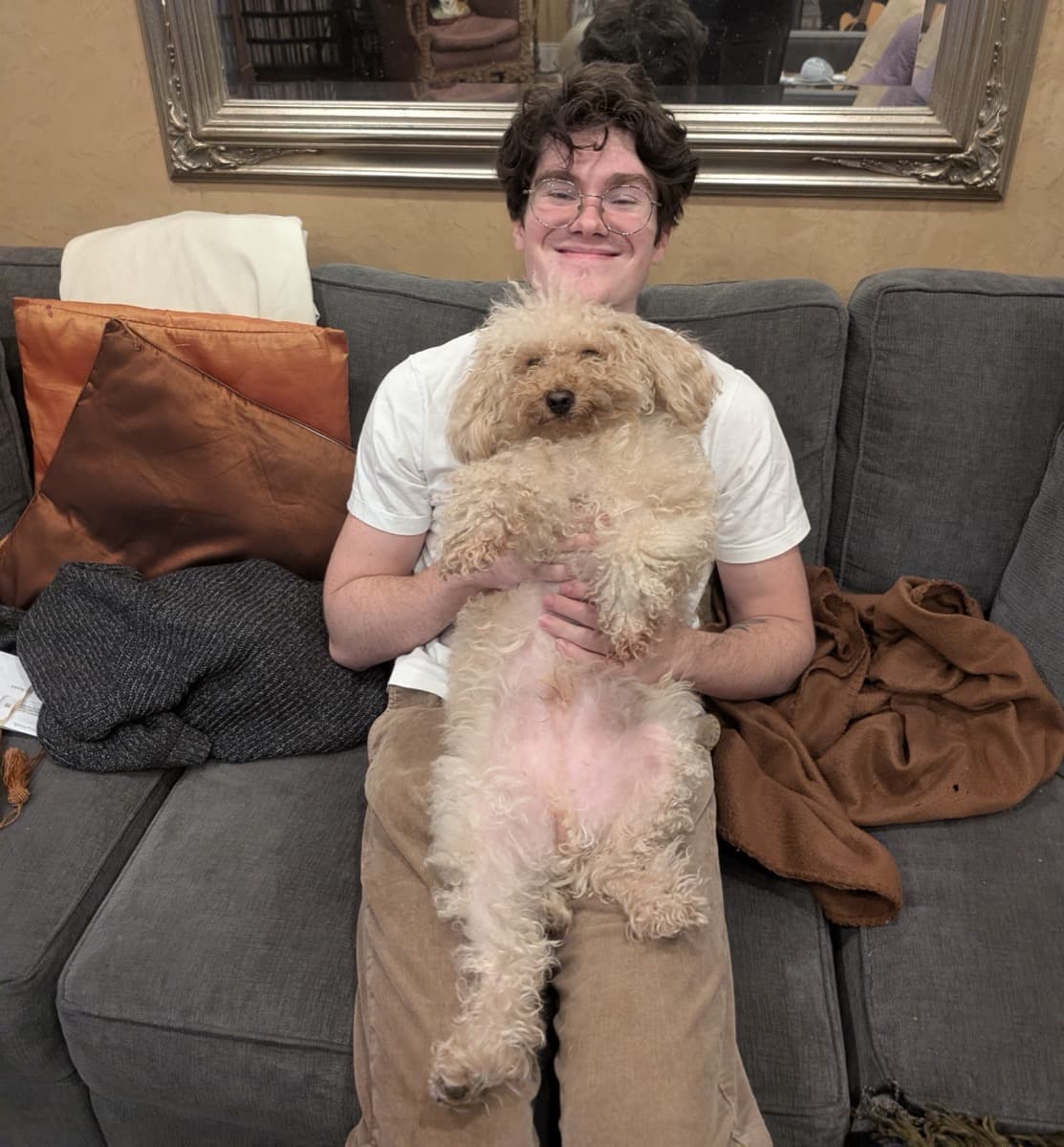 Michael grinning on a couch, holding a very relaxed fluffy dog